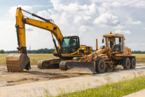 The excavator and the grader stand side by side against the blue sky. Heavy construction earthmoving equipment. Construction of roads and underground communications. Construction industry.