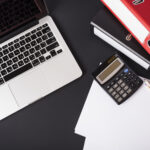 overhead-view-laptop-file-folders-calculator-pencils-paper-black-background